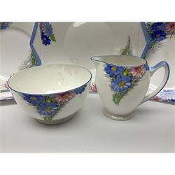 Shelley Strand shaped tea wares, decorated with blue and pink daisies upon a white ground, comprising four teacups, four saucers, three tea plates, milk jug, sugar bowl and cake plate, all with printed green mark beneath and painted pattern no 12216