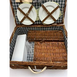 A wicker picnic hamper with accompanying contents. 