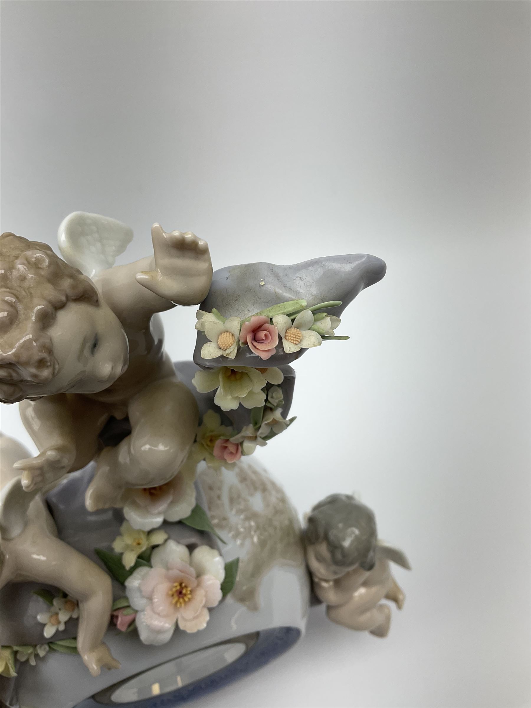 A Lladro mantel clock modelled as a globe with inset clock, surmounted by four putti and floral garlands, with blue printed mark and impressed 5973 beneath, H29cm.
