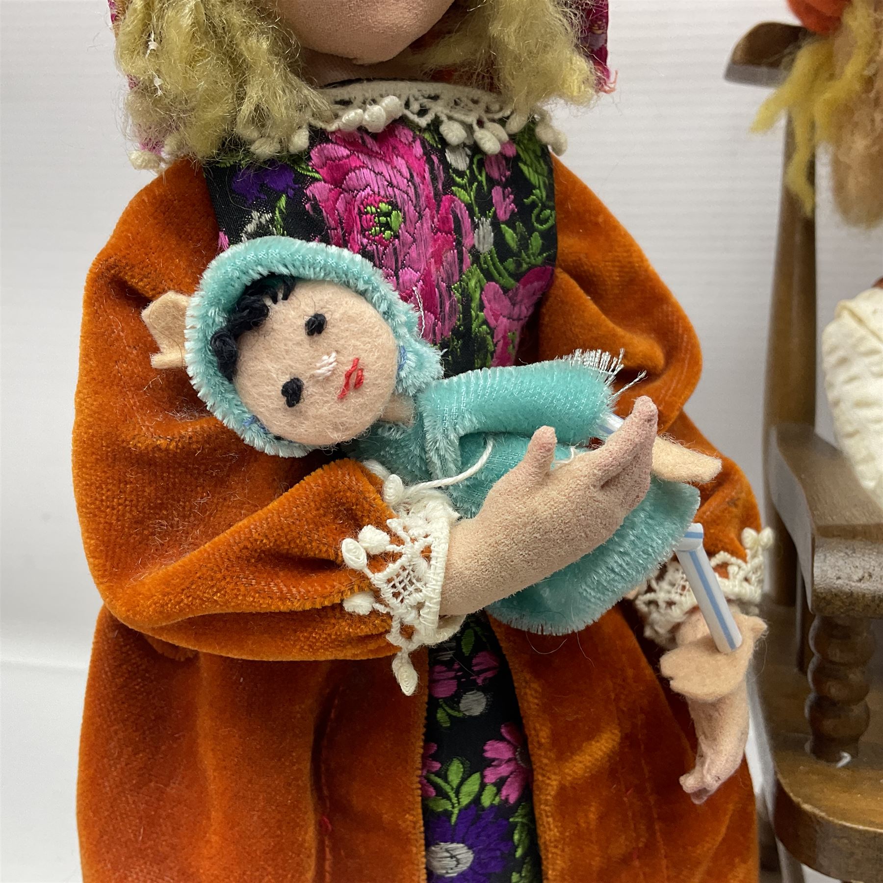 Anna Meszaros Hungary - three hand made needlework figurines - 'The Cobbler' as a child seated in a wooden rocking chair working on a removed boot H24cm; young girl standing crying holding a doll with broken head H32cm; and young girl in long dress and bonnet standing holding a doll H27cm (3)  Auctioneer's Note: Anna Meszaros came to England from her native Hungary in 1959 to marry an English businessman she met while demonstrating her art at the 1958 Brussels Exhibition. Shortly before she left for England she was awarded the title of Folk Artist Master by the Hungarian Government. Anna was a gifted painter of mainly portraits and sculptress before starting to make her figurines which are completely hand made and unique, each with a character and expression of its own. The hands, feet and face are sculptured by layering the material and pulling the features into place with needle and thread. She died in Hull in 1998.