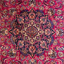 North East Persian Mashad hand-knotted carpet, rich madder red field with central cusped foliate medallion with issuing scrolling arabesques, palmettes, and floral sprays, enclosed within a broad indigo main border of bold palmettes, between multiple guard stripes, with cotton fringe ends 