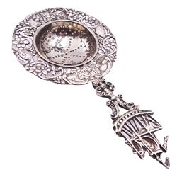 Early 20th century silver tea strainer, the circular pierced bowl with embossed and pierced surround depicting birds, huts and windmills amidst flower heads and C scrolls, with figural stem with terminal modelled as a three-masted ship, hallmarked Berthold Hermann Muller, London import 1915, also marked 1925, L13.5cm, approximate weight 1.50 ozt (46.9 grams)