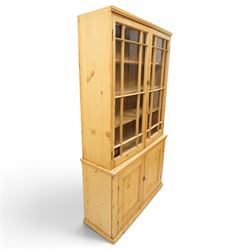 19th century pine glazed bookcase cupboard, twin astragal glazed doors with stained glass corner panels, enclosing fixed shelves, the lower section fitted with two panelled cupboard doors enclosing single shelf, on plinth base