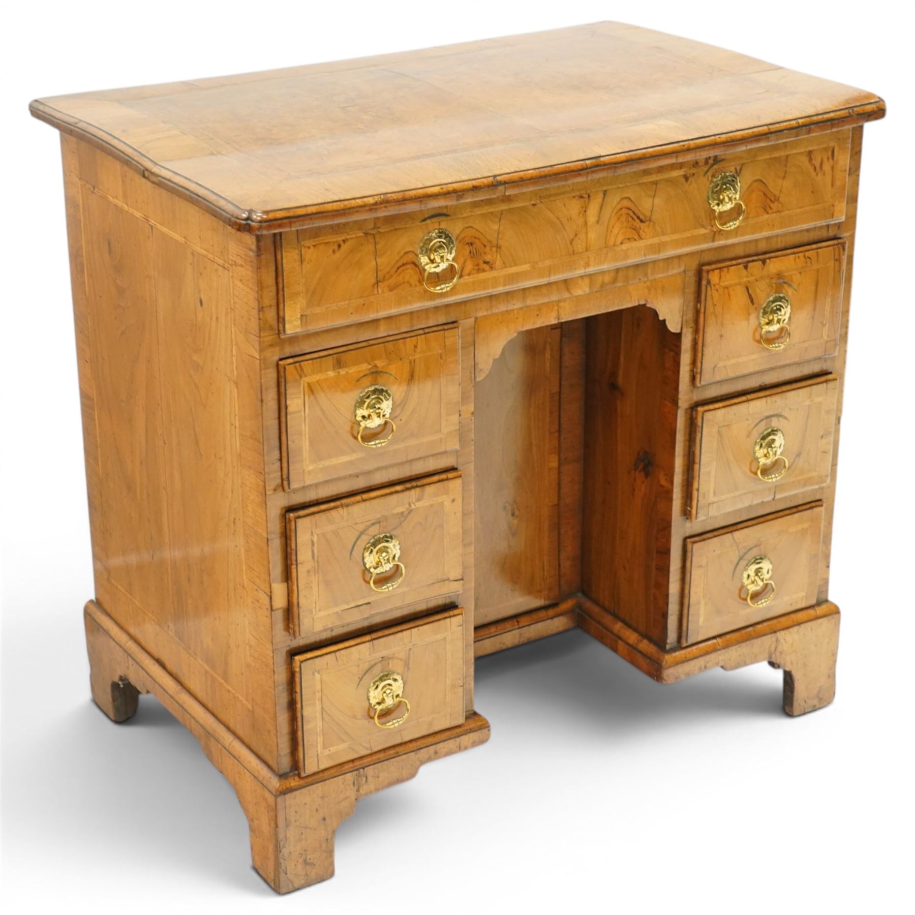 George III figured and burr walnut kneehole desk, the shaped rectangular top with feather and crossbanding surrounded by a moulded edge, fitted with single frieze drawer over three graduating drawers to each side, flanking a central recessed cupboard, lower moulded edge on bracket feet
Provenance: Kirkham Hall