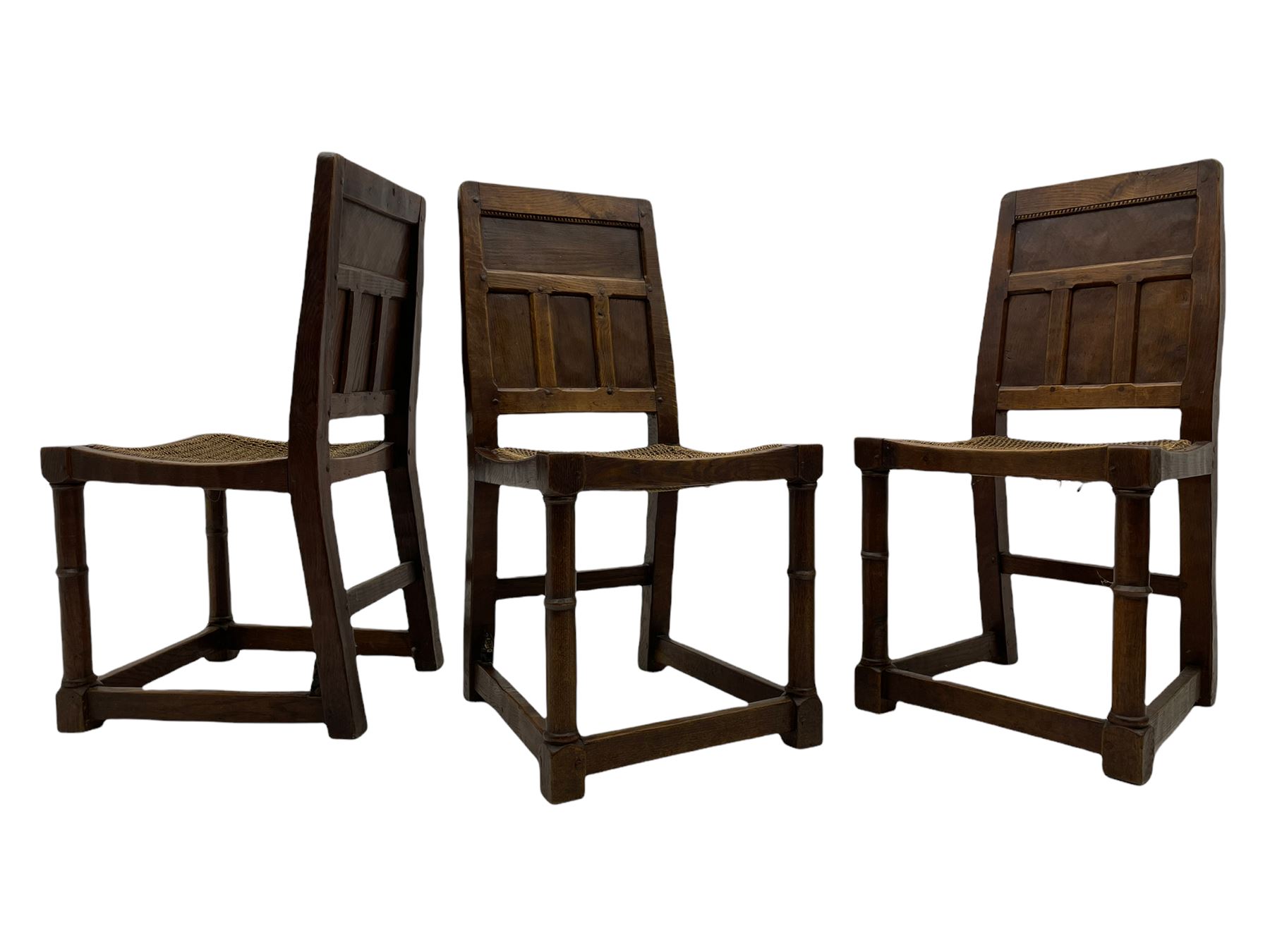 'Gnomeman' set of three oak dining chairs, panelled backs over curved seat rails with drop in rope rush seats, turned front supports with collar joined by plain stretchers, two with carved seated gnome figures, painted

Provenance - This collection of early 'Gnomeman' furniture comes to us directly from the Whittaker family. The pieces were made by the vendor's father Thomas Whittaker in the 1930/40s for his own use. During this time, he lived in York and made items for himself and friends. Whittaker adopted the gnome as a signature and trademark after his move to Littlebeck, Whitby.