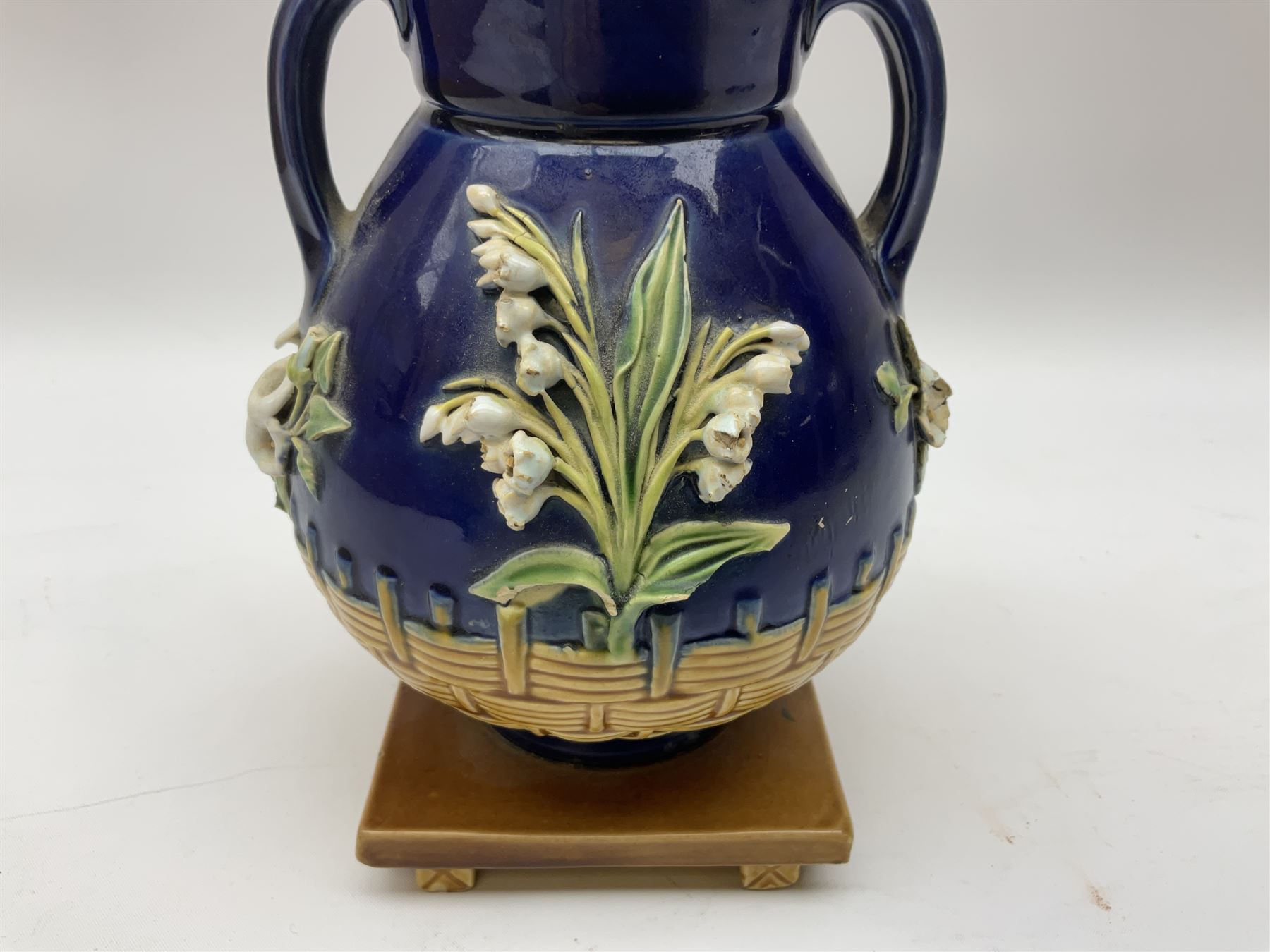 Minton majolica vase, the squat body with twin handles, with part osier moulding and applied Spring flowers against a cobalt blue ground, upon integral square base, impressed beneath Minton 1316, H16.5cm