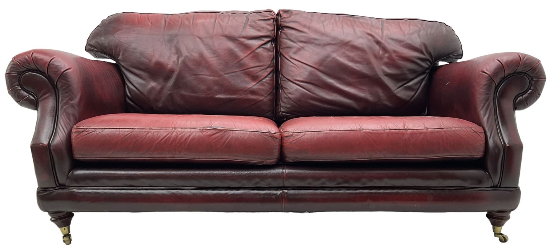 Thomas Lloyd - three-piece lounge suite, comprising of traditional shape two seat sofa (W190cm H80cm) and a pair of wingback armchairs (W100cm H91cm), each with rolled arms over turned supports with brass castors, upholstered in oxblood red leather