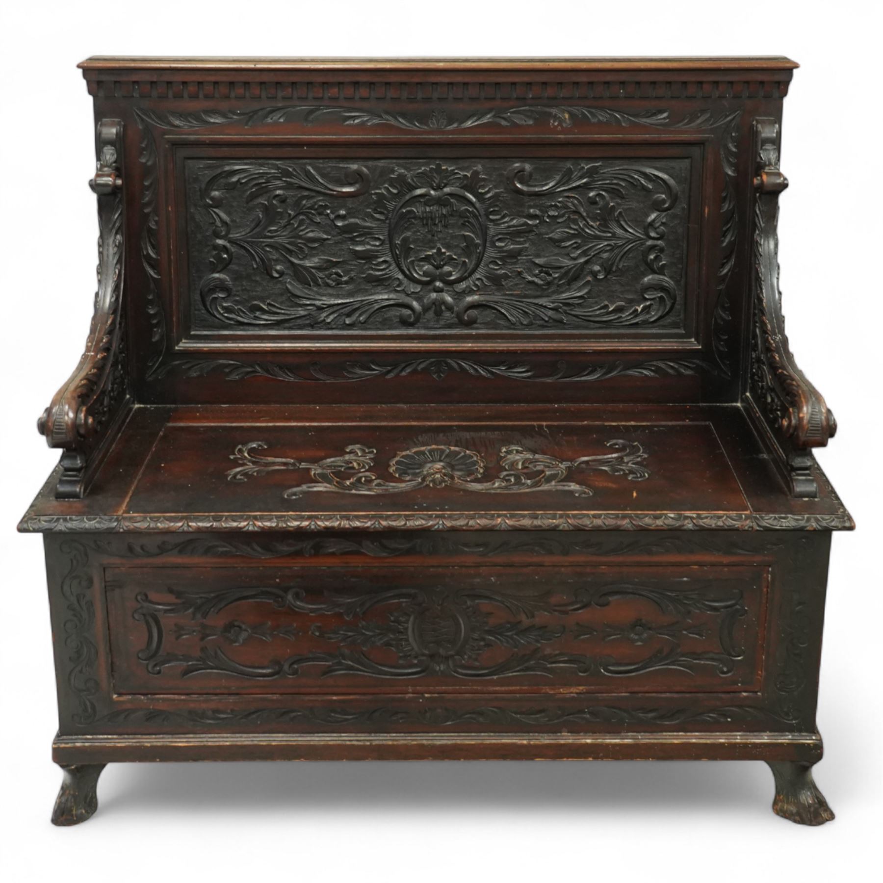 Late Victorian carved oak hall bench, the panelled back deeply carved with scrolling acanthus and central cartouche, hinged seat with foliate and shell motifs, scroll carved arm supports, on short cabriole front legs