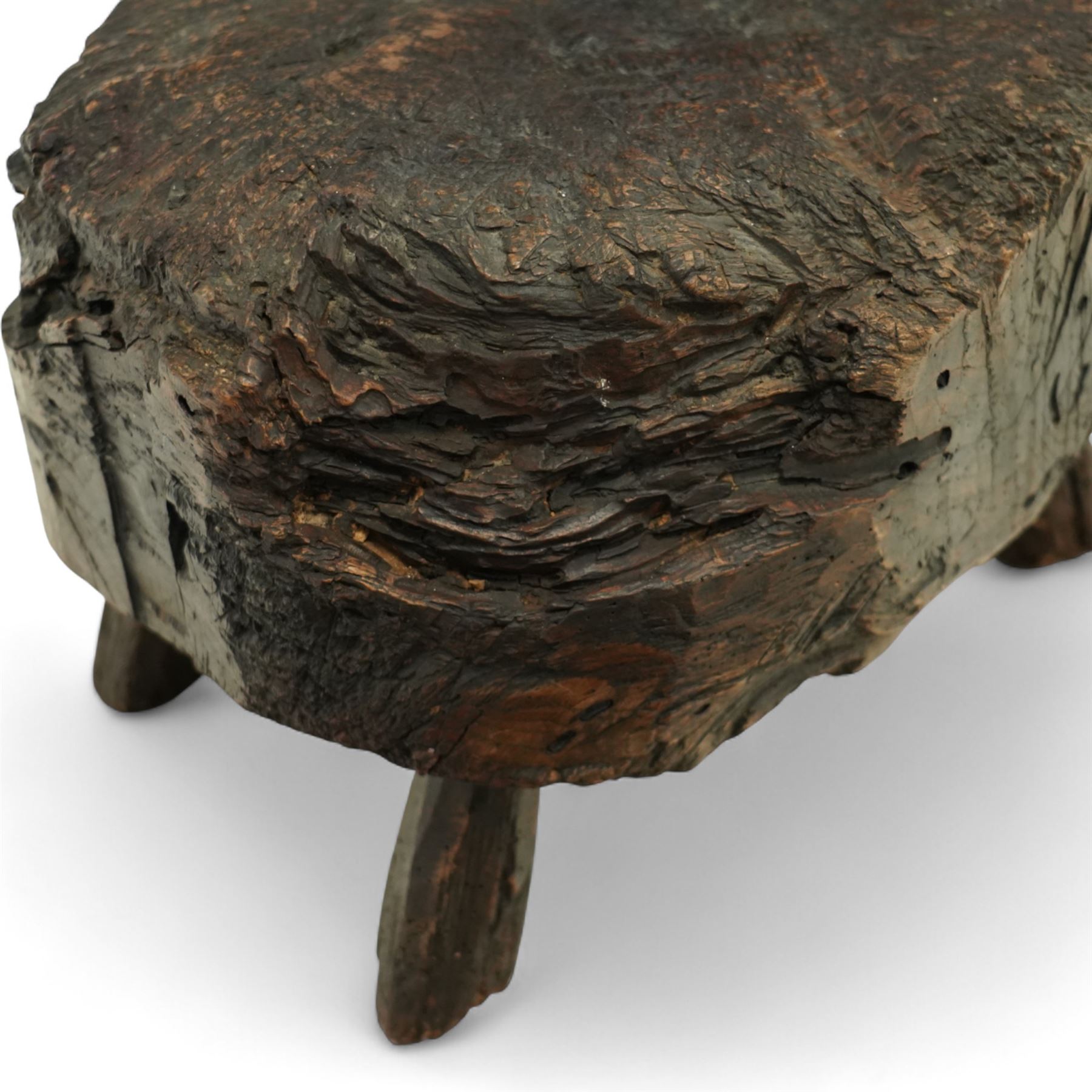 Rustic bog oak stool of oval form with a single solid section with a deeply patinated and textured surface, raised on three tapered stick legs, possibly Irish 