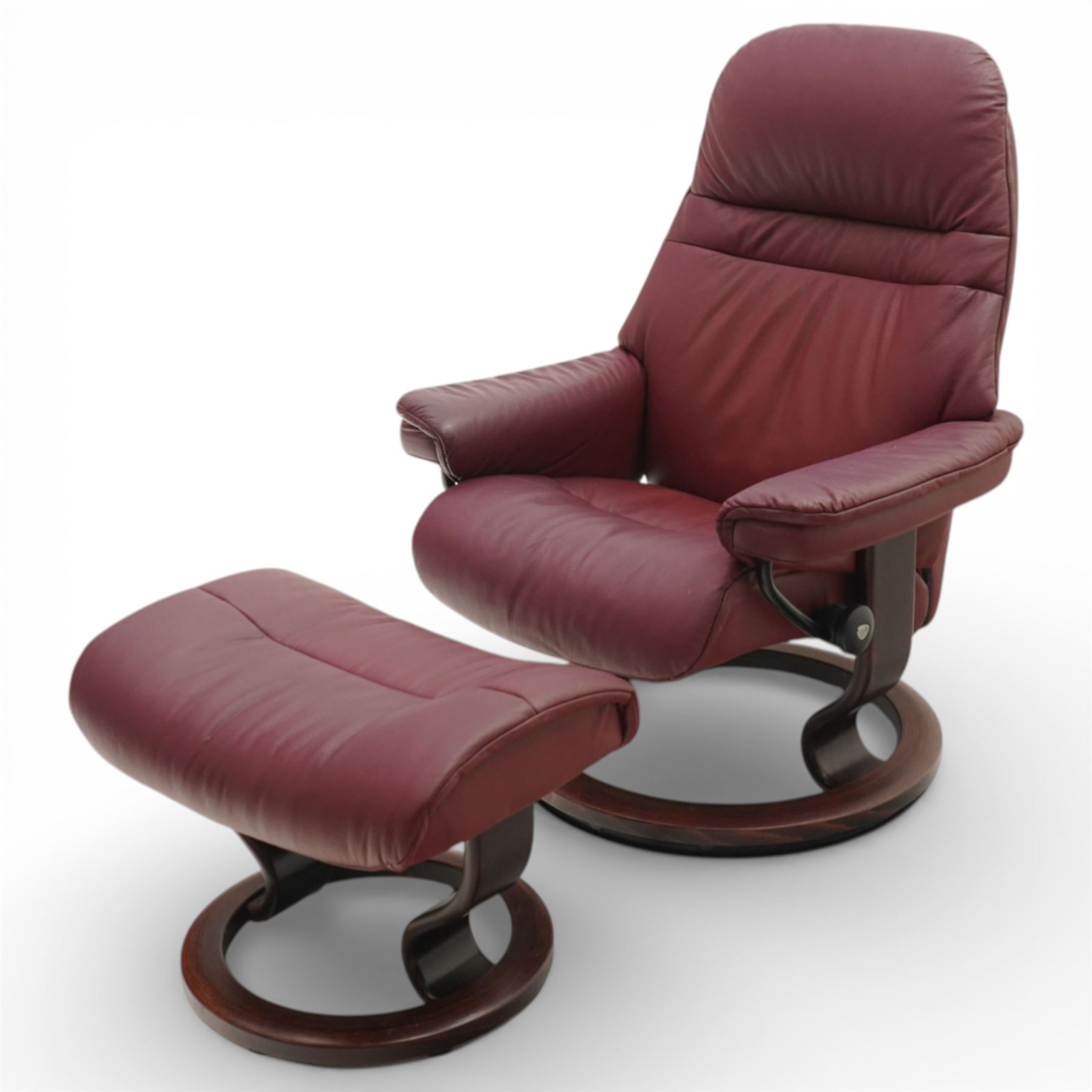Ekornes - Stressless reclining armchair and matching footstool, upholstered in oxblood leather with padded headrest and segmented back cushion, shaped armrests with exposed adjustment handles, raised on stained laminated beech circular swivel base, the conforming stool on matching ring base