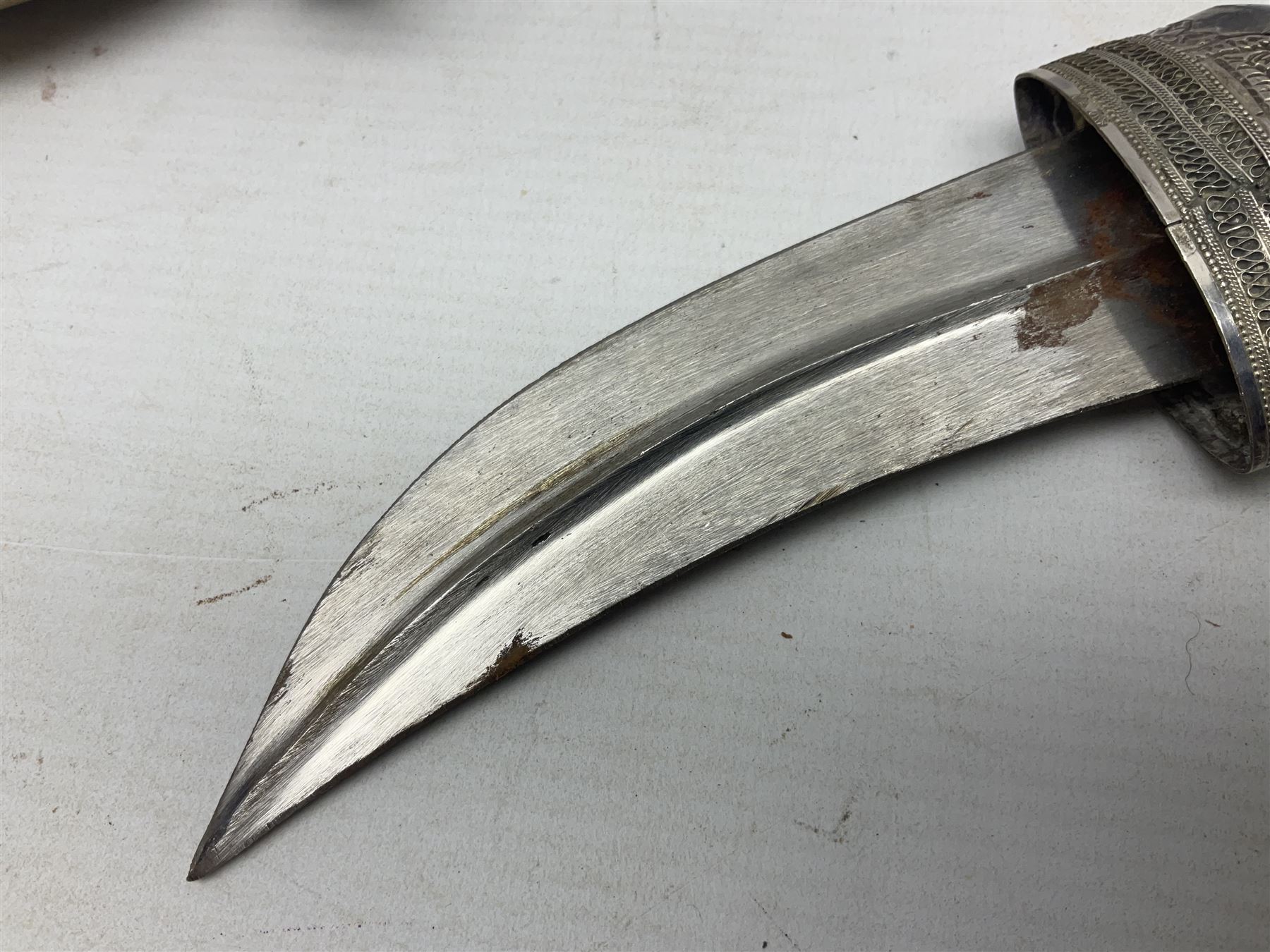 Omani Khanjar dagger, the 12.5cm curved blade with pronounced medial rib to either side, waisted horn style hilt with dome shaped pommel and inlaid pique work; in an intricately filigree decorated white metal scabbard with rings woven into the belt mount L25cm overall