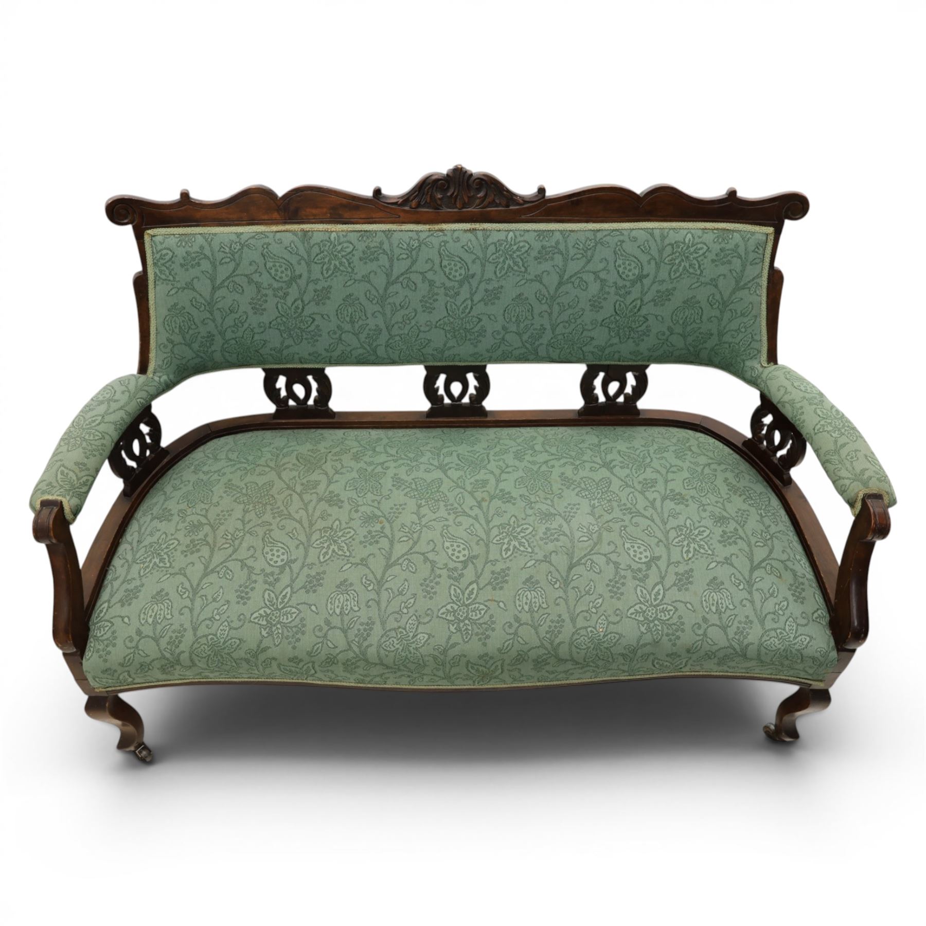 Edwardian mahogany framed sofa, shaped cresting rail with scroll terminals and carved foliate pediment, upholstered back and swept arms in green foliate fabric, pierced splat supports, serpentine front seat rail, on cabriole supports terminating in castors