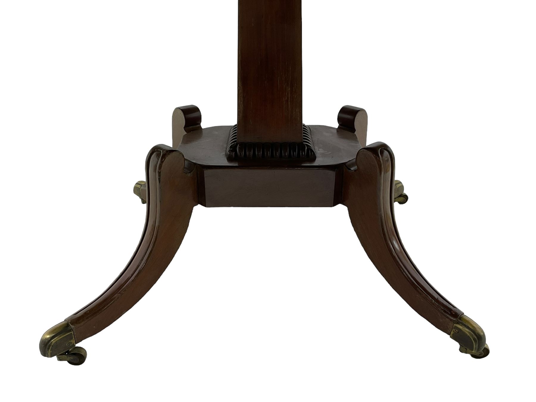 Regency mahogany dining table, rectangular top with rounded corners and reeded edge, raised on square pedestal with platform, terminating to sabre supports with brass cups and castors