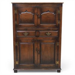  Late 20th century oak four door cupboard in the manner of Titchmarsh and Goodwin, rectangular plank top above two pairs of fielded panel doors with shaped raised panels, central arrangement of a brushing slide above two short drawers with brass swan neck handles and pierced backplates, enclosed by further pair of panelled cupboard doors, fitted with brass butt hinges and turned wooden knobs, raised on plinth base