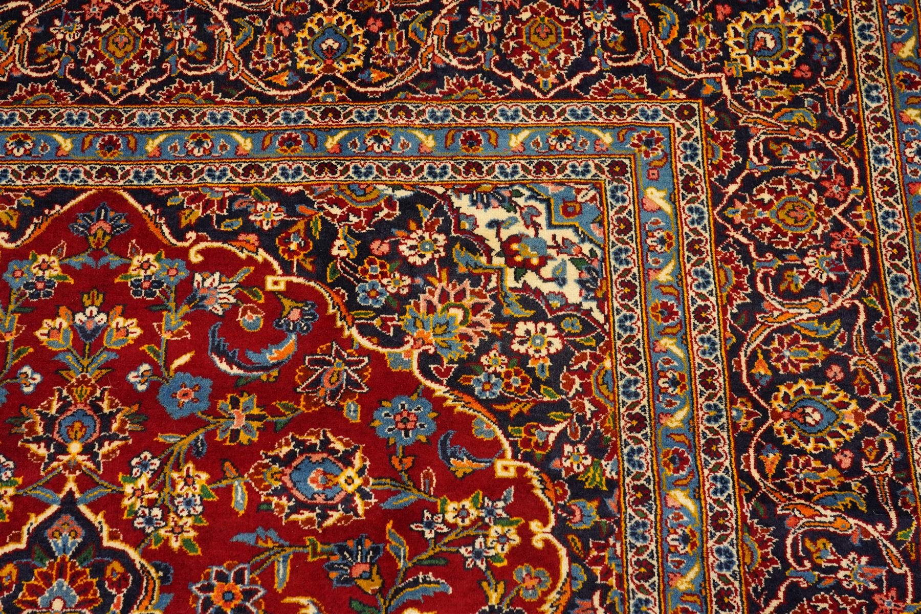 Central Persian Kashan hand-knotted carpet, crimson field with central cusped medallion in ivory, pale blue and indigo, issuing a network of scrolling arabesques, palmettes, and floral sprays, with conforming spandrels, main border of scrolling vinery and stylized palmettes, framed by multiple guard borders, with cotton fringe ends 