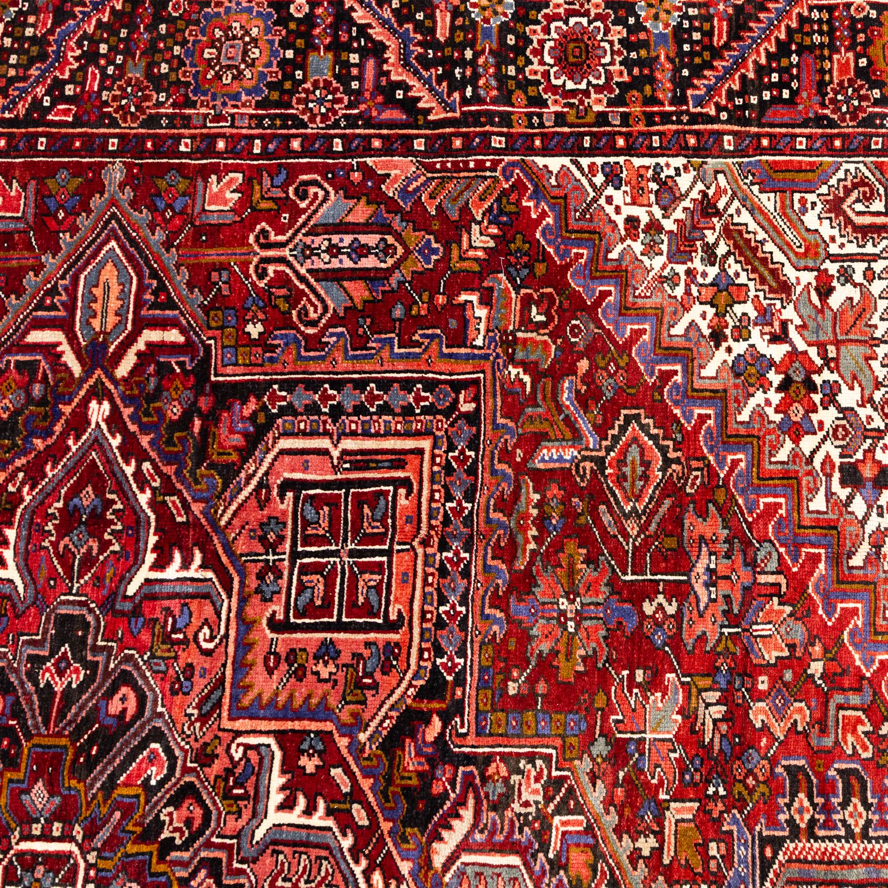 North West Persian Heriz hand-knotted carpet, brick red field, with large central angular star medallion with stepped outlines, surrounded by geometric floral devices and stylized rosettes, with corresponding corner spandrels, enclosed by a bold geometric main border with multiple guard stripes, with cotton fringe ends 