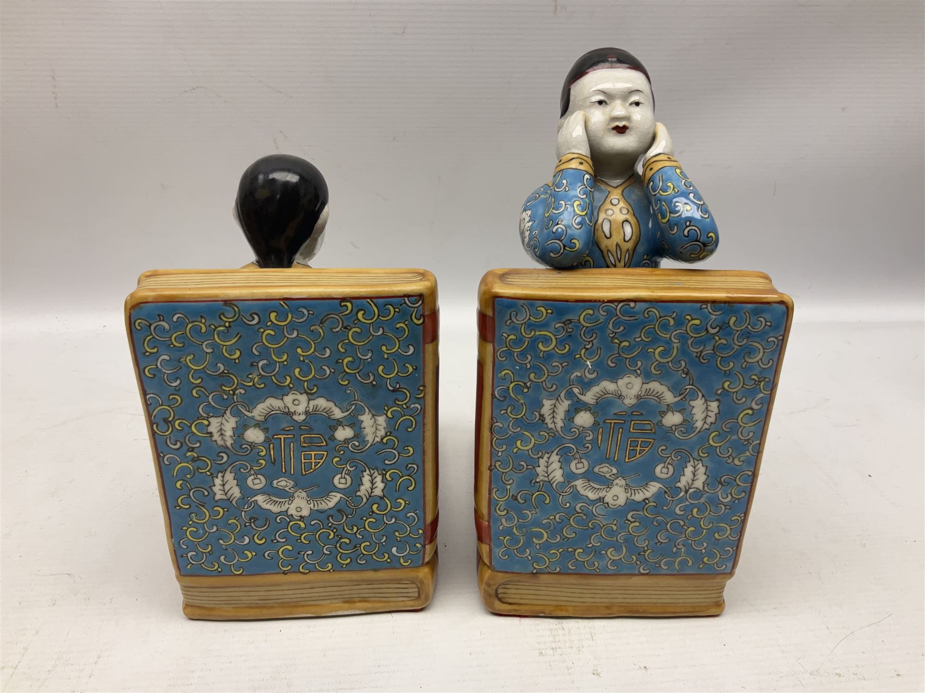 Pair of 20th century Chinese figural bookends, modelled as children in traditional blue dress sat reading and kneeling upon stacks of books, H22cm