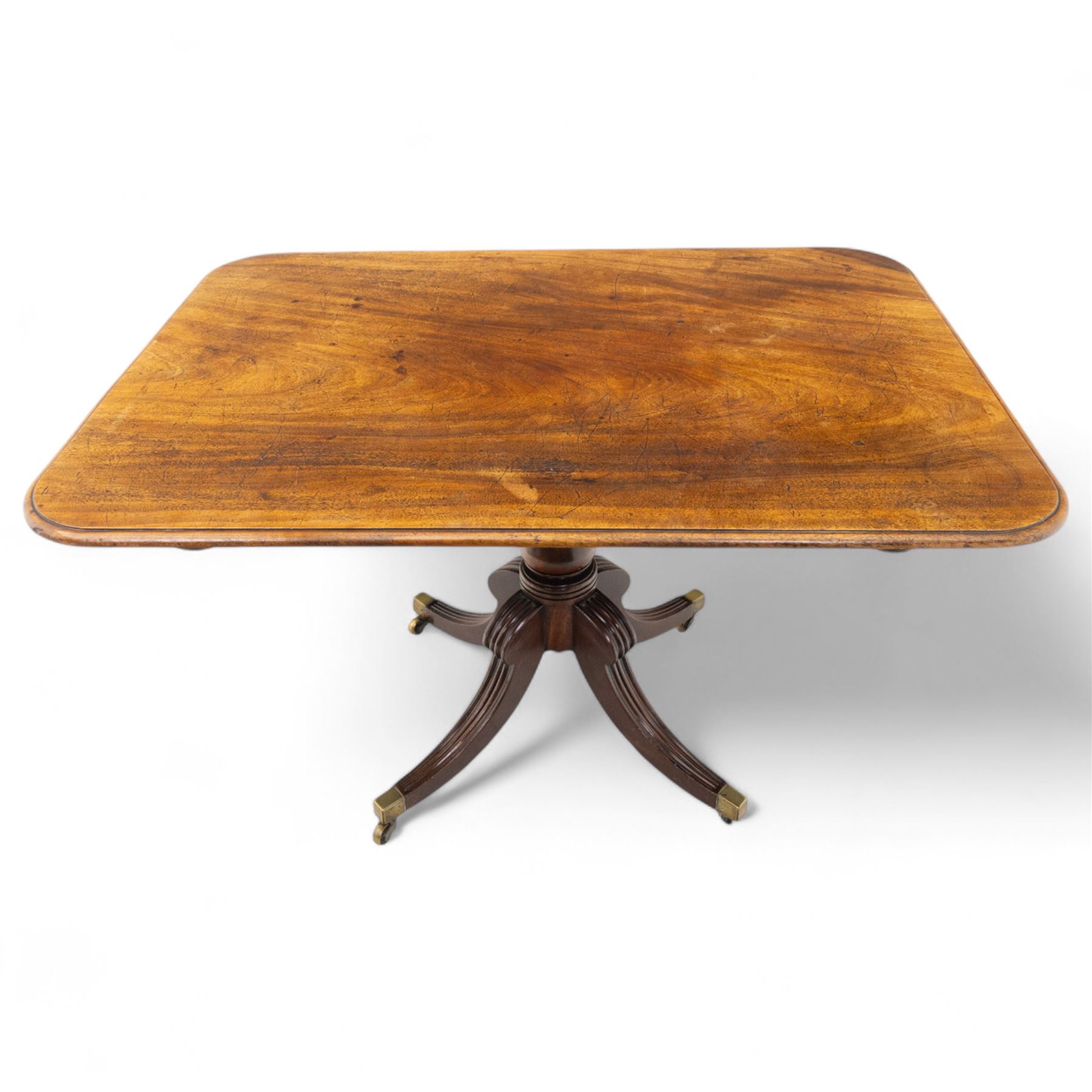 George IV mahogany breakfast table, rectangular tilt-top with reeded edge, rounded corners, supported on a turned column and raised on a quadripartite base with reeded down-swept legs terminating in brass cap castors