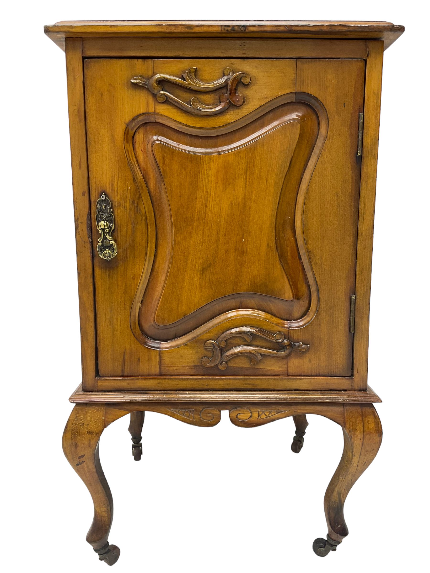 Edwardian Art Nouveau walnut bedside cabinet, raised broken swan neck back with carved flower heads, single fielded panelled door enclosing single shelf, raised on cabriole supports with ceramic castors