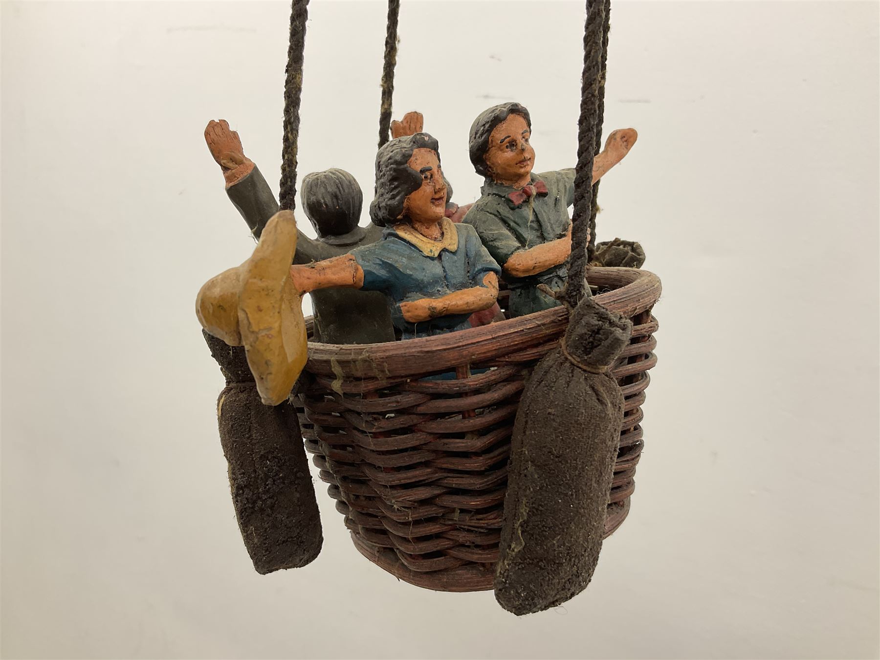 Painted wooden hanging model of a hot air balloon group, the balloon above a wicker basket complete with sandbags and figures, together with a similar example with a clown figure below, H68cm