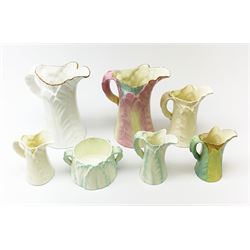 A group of six Royal Worcester leaf moulded porcelain jugs, largest with pink toned glaze, H17.5cm, plus a similarly modelled twin handled sucrier. (7).