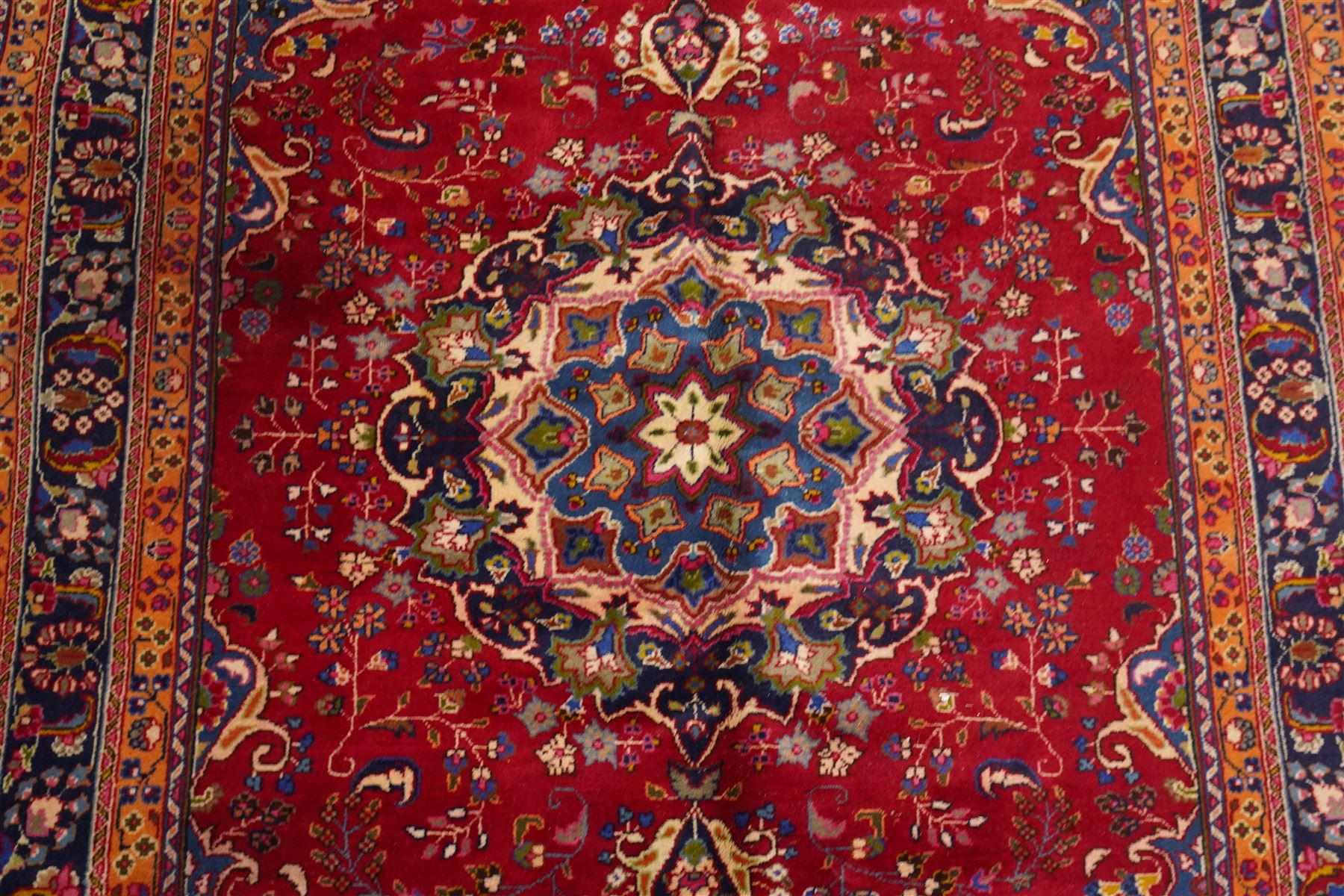 Persian Kashan hand-knotted rug, madder red ground centred by circular floral medallion with pendants, surrounded by scrolling vines, palmettes and flowerheads, dark navy spandrels, enclosed by dark navy floral border with multiple guard stripes