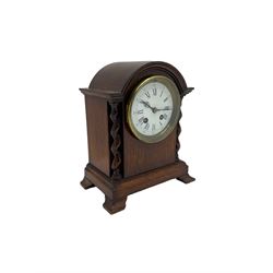 Early 20th century oak cased mantle clock, with a break arch top and barley twist columns,  low plinth raised on oak bracket feet, with a French eight-day movement striking the hours and half-hours on a bell, enamel dial with gothic numerals and steel fleur di Lis hands. With Pendulum.

