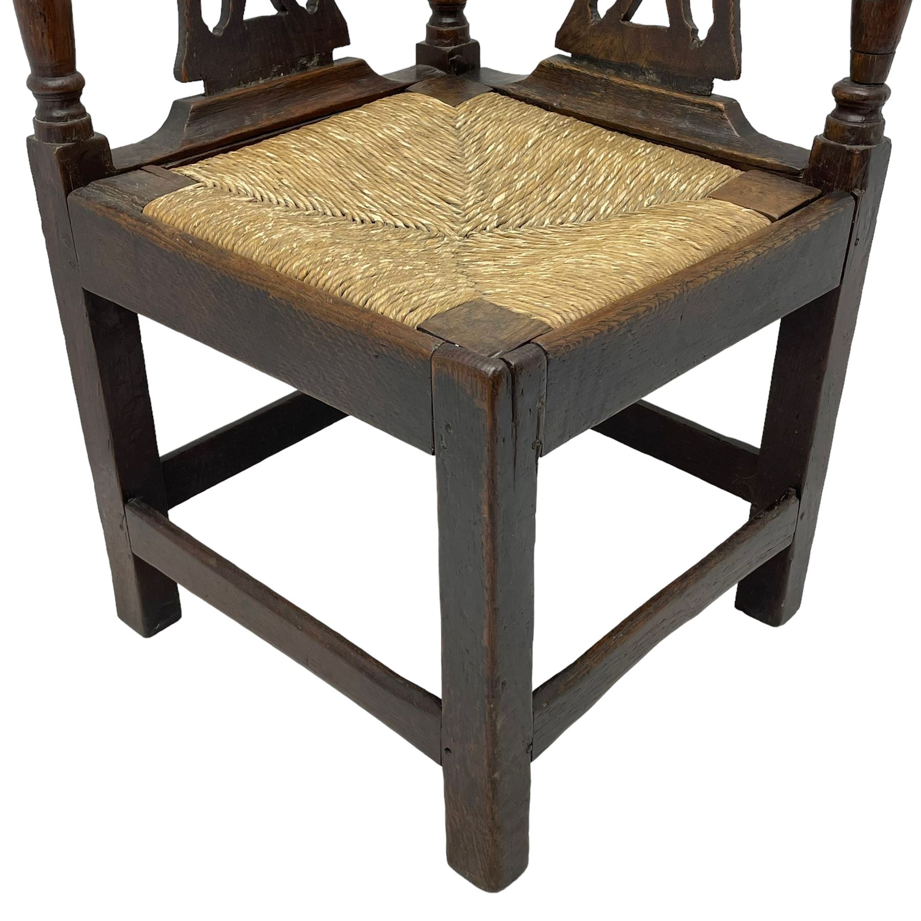 18th century country elm and oak corner chair, the shaped cresting rail terminating to swept arm resets, supported by turned columns and pierced shaped splats, over a drop-in rush seat, raised on square supports united by box stretcher