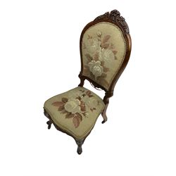Victorian simulated rosewood framed nursing chair, the cresting rail carved with scrolls and foliage, upholstered in floral needlework cover, on cabriole supports with brass and ceramic castors