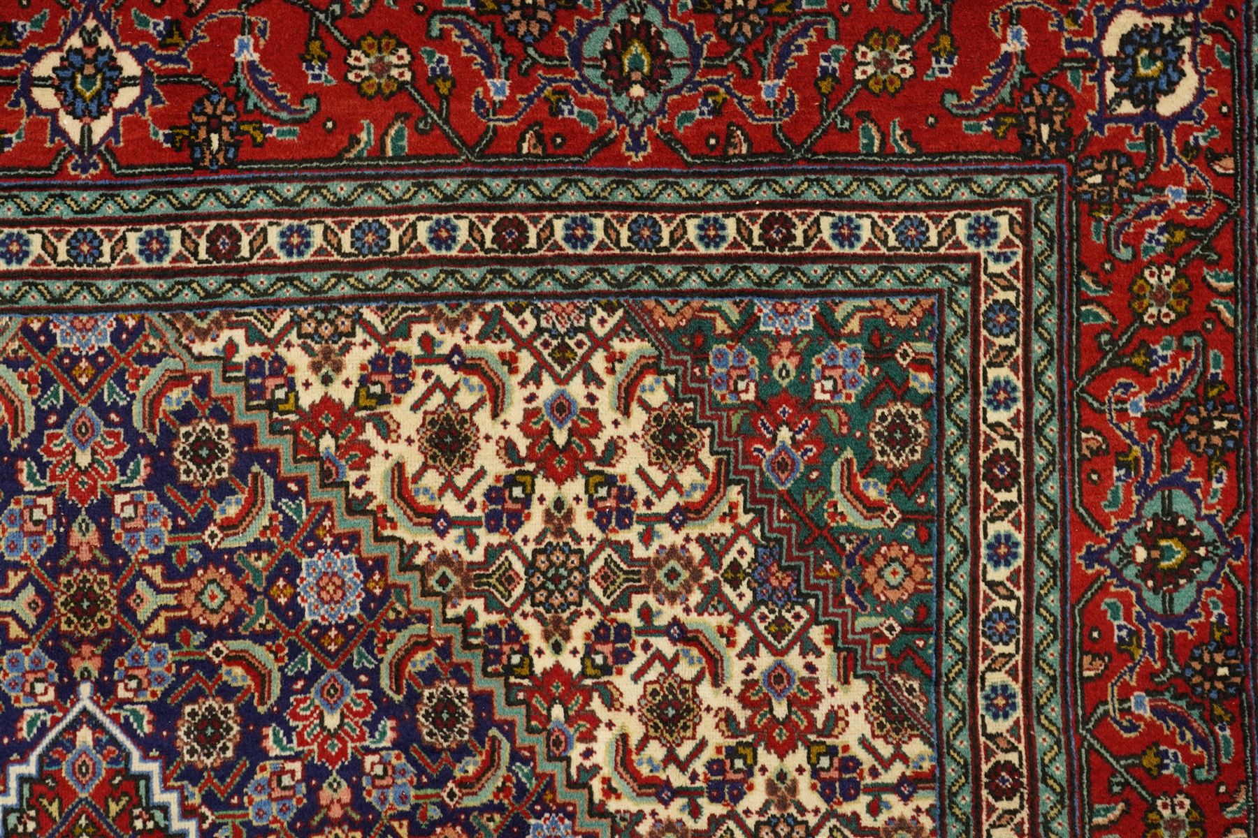 North West Persian Tabriz hand-knotted rug, ivory field with a central lozenge shaped medallion in indigo and madder red, issuing an ornamented arrangement of Herati style motifs, rosettes and angular floral elements, conforming spandrels on an ivory ground, main border in madder red with stylized vinery and palmettes, flanked by multiple guard border, with cotton fringe ends 