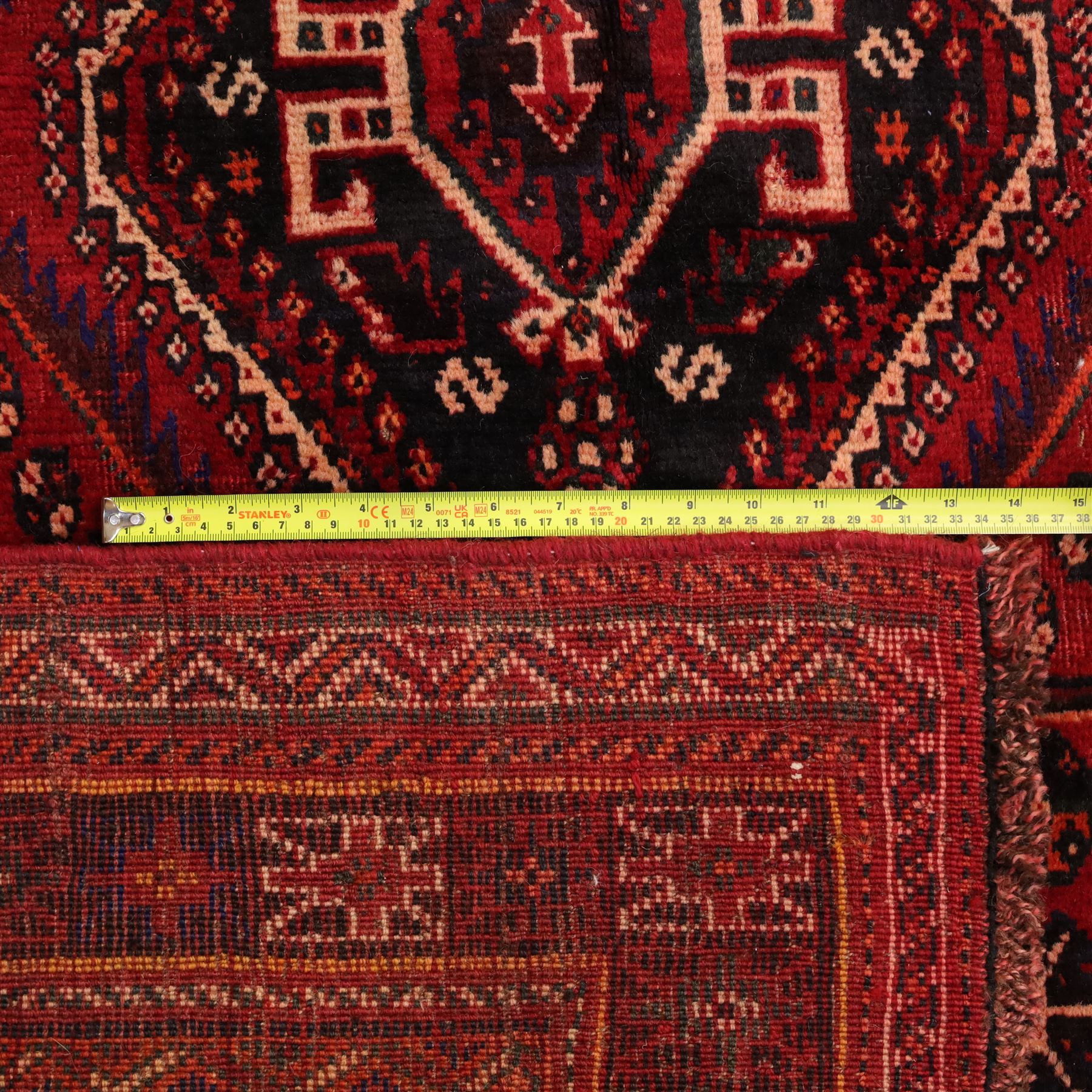 South West Persian Qashqai hand-knotted rug, madder red field with a large stepped diamond medallion with scattered geometric devices and indigo spandrels filled with geometric motifs, framed by multiple narrow guard borders and broad main border, wool fringe ends 