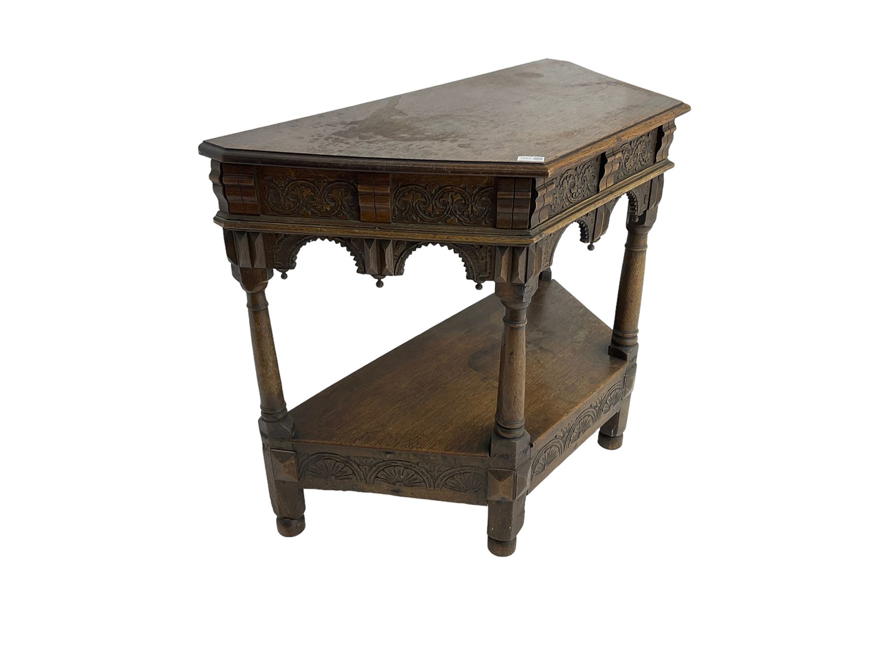 Jacobean design carved oak side or credence table, demi-heptagon top with moulded edge, frieze carved with foliate C-scroll design above ornate arcade carved apron, under-tier united by ring turned pilisters, lower frieze carved with repeating lunettes