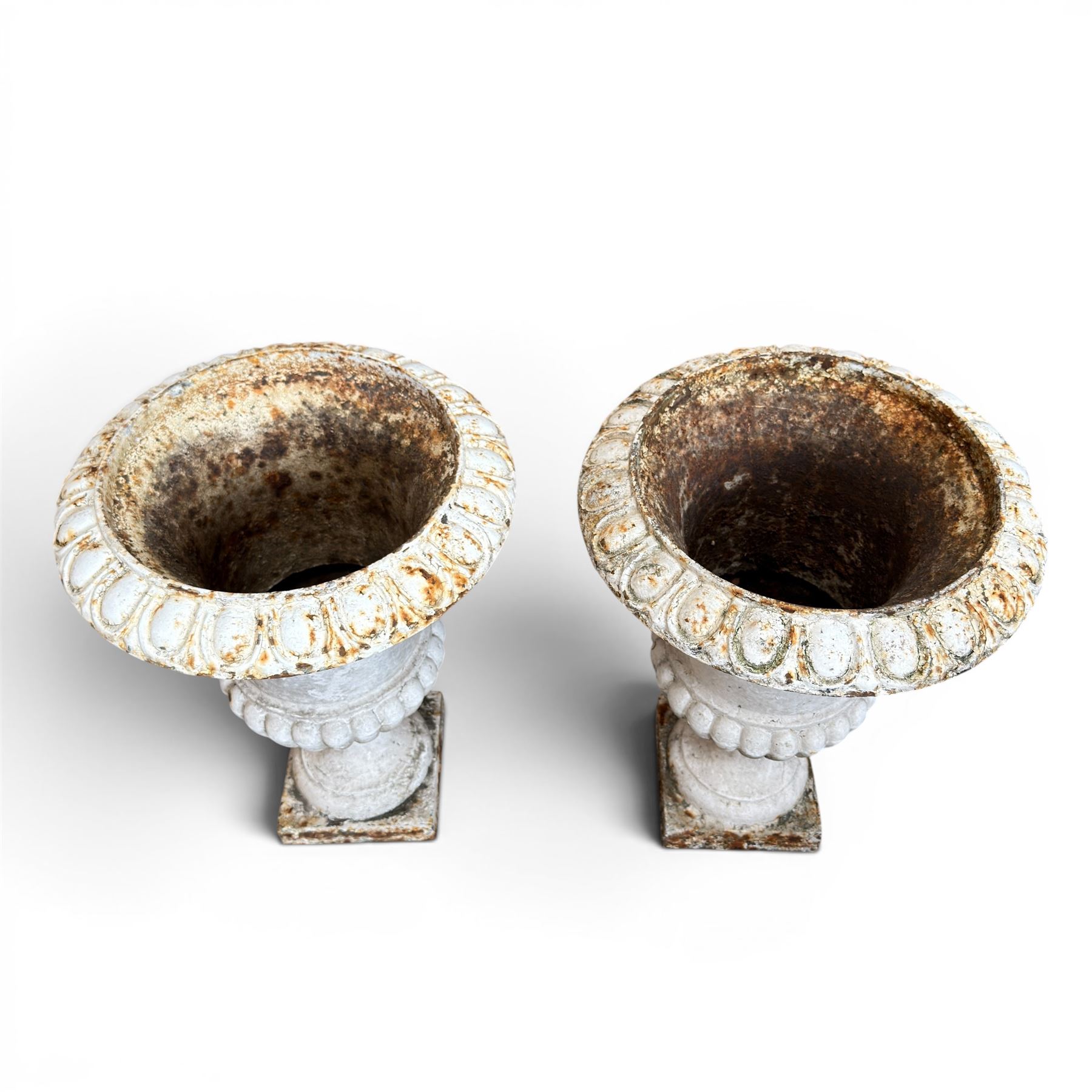Pair of Victorian revival cast iron garden urns, egg and dart rim, tapering column with gadrooned waist, on square base, finished in distressed white paint