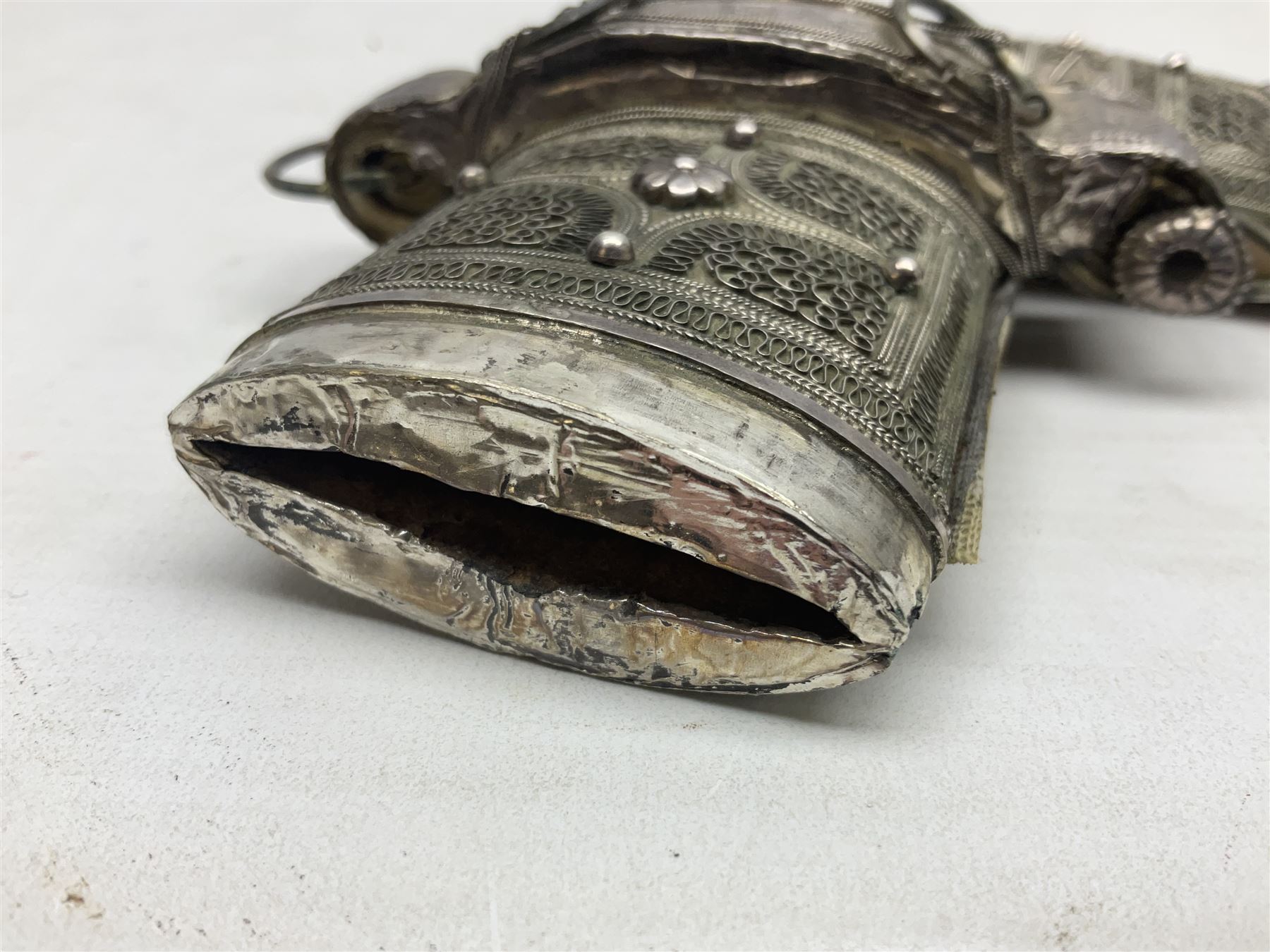 Omani Khanjar dagger, the 12.5cm curved blade with pronounced medial rib to either side, waisted horn style hilt with dome shaped pommel and inlaid pique work; in an intricately filigree decorated white metal scabbard with rings woven into the belt mount L25cm overall