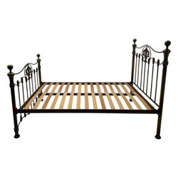 Victorian design king size brass bed frame, featuring an arched headboard and footboard with intricate cast floral and scrollwork centre motifs, flanked by cylindrical supports with ball finials and decorative collars, raised on rounded feet, with a slatted wooden base