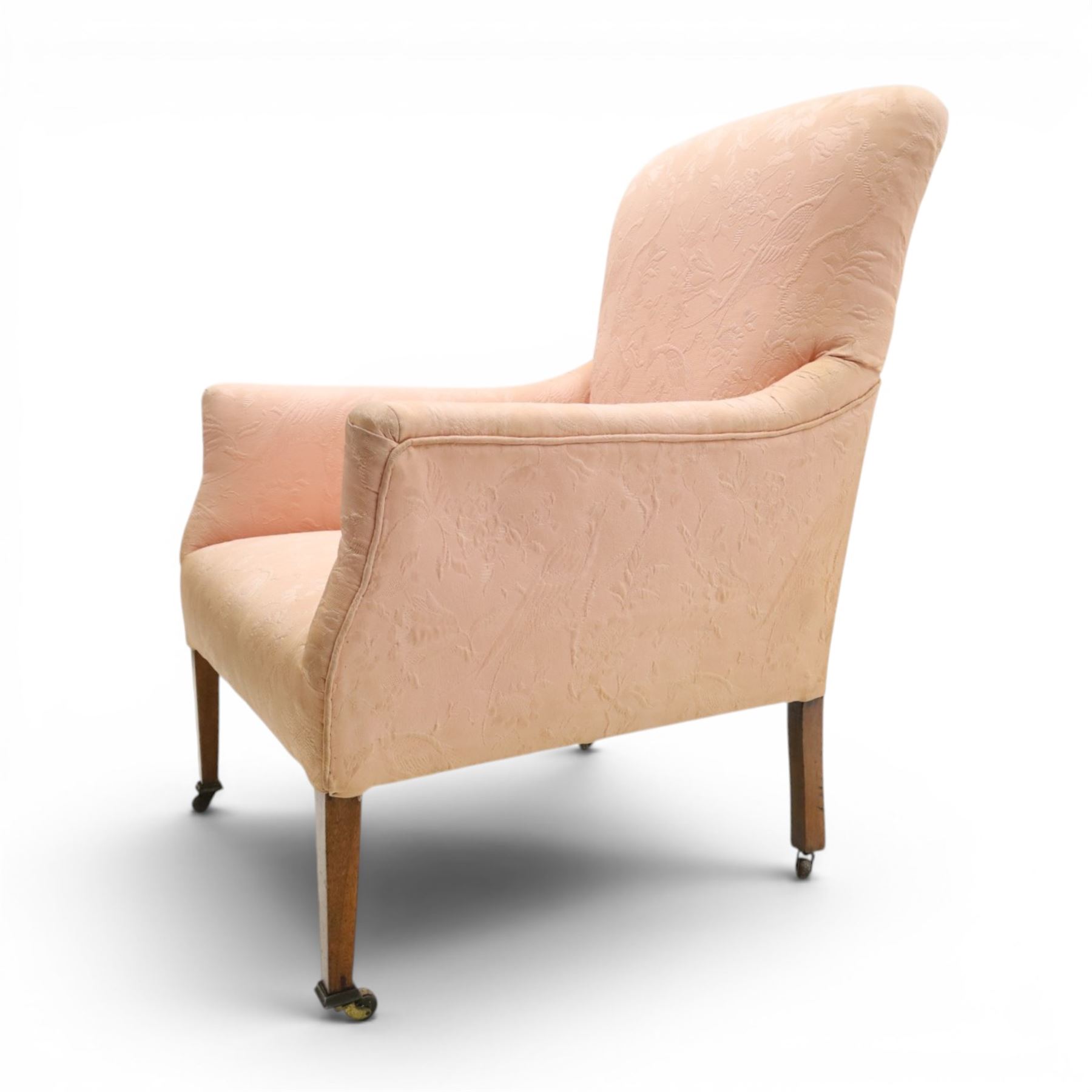 Edwardian mahogany framed armchair of traditional shape, high sprung back and seat over squared padded arms, upholstered in foliate patterned pale pink upholstery, on square tapering supports with brass castors