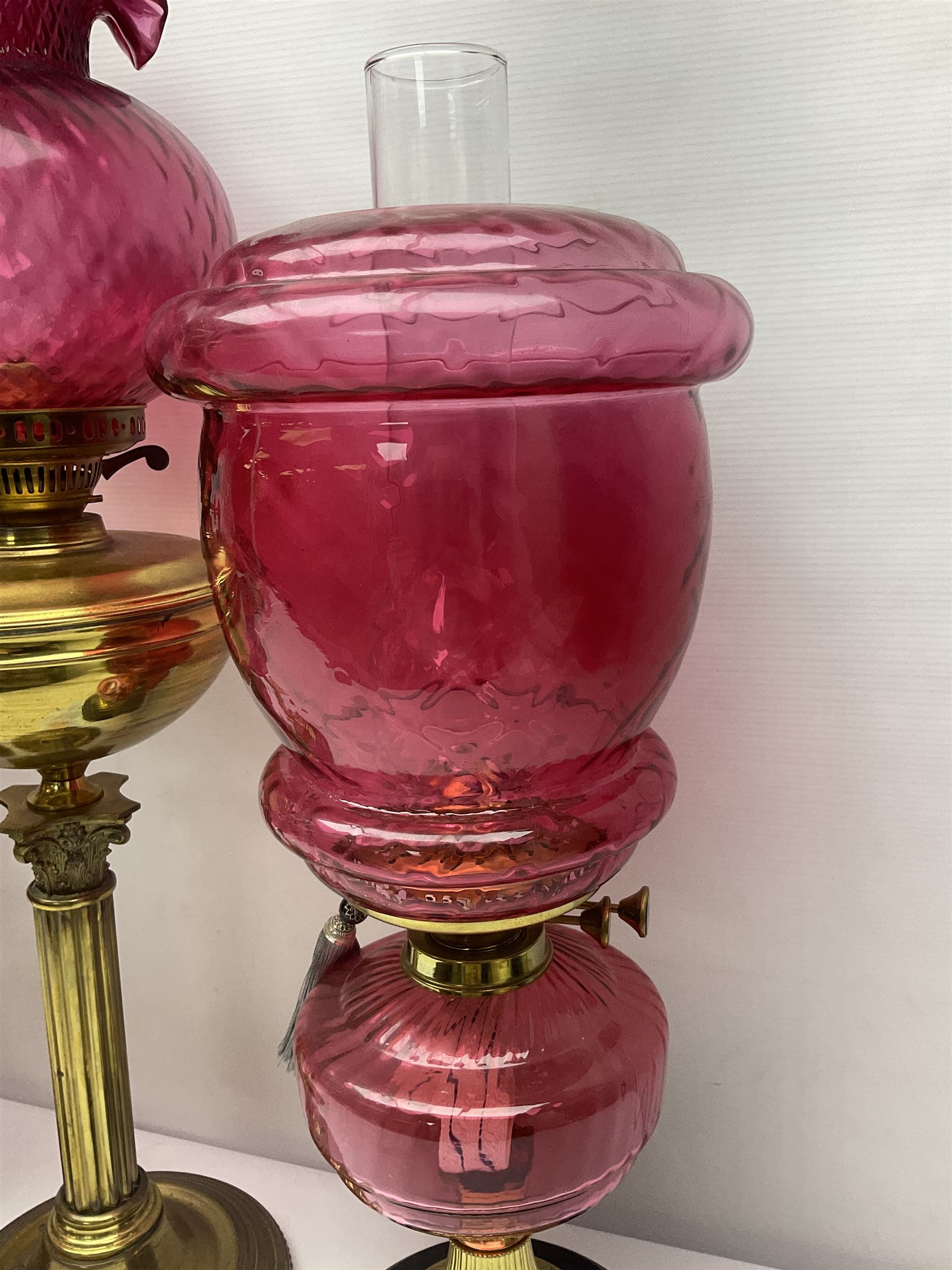 Victorian cast brass oil lamp, with fluted pink glass shade, together with two smaller brass oil lamps with pink shades and reservoirs and a pair of oil lamps, the bases modelled as putti, with pink glass reservoir  and frosted shades, tallest H70cm