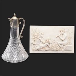 Composite plaque, depicting Sprites in a garden, with inset 'Arts and Commerce Promoted' medallion to reverse, 20cm x 33cm; together with a moulded glass Claret jug with silver plated mount H30cm 