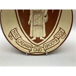 20th century Dewi Bowen Welsh studio pottery plate, decorated with the Merthyr Tydfil coat of arms, depicting Saint Tydfil beneath a banner inscribed with the motto Nid Cadarn Ond Brodyrdde (No strength but in fellowship), signed and dated 1972 verso, D29cm.