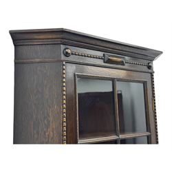 Early 20th century oak corner display cabinet, the moulded canted cornice over a single glazed door with geometric astragal bars, shelved interior, the lower tier forming a triangular platform, raised on four barley-twist supports united by shaped brackets