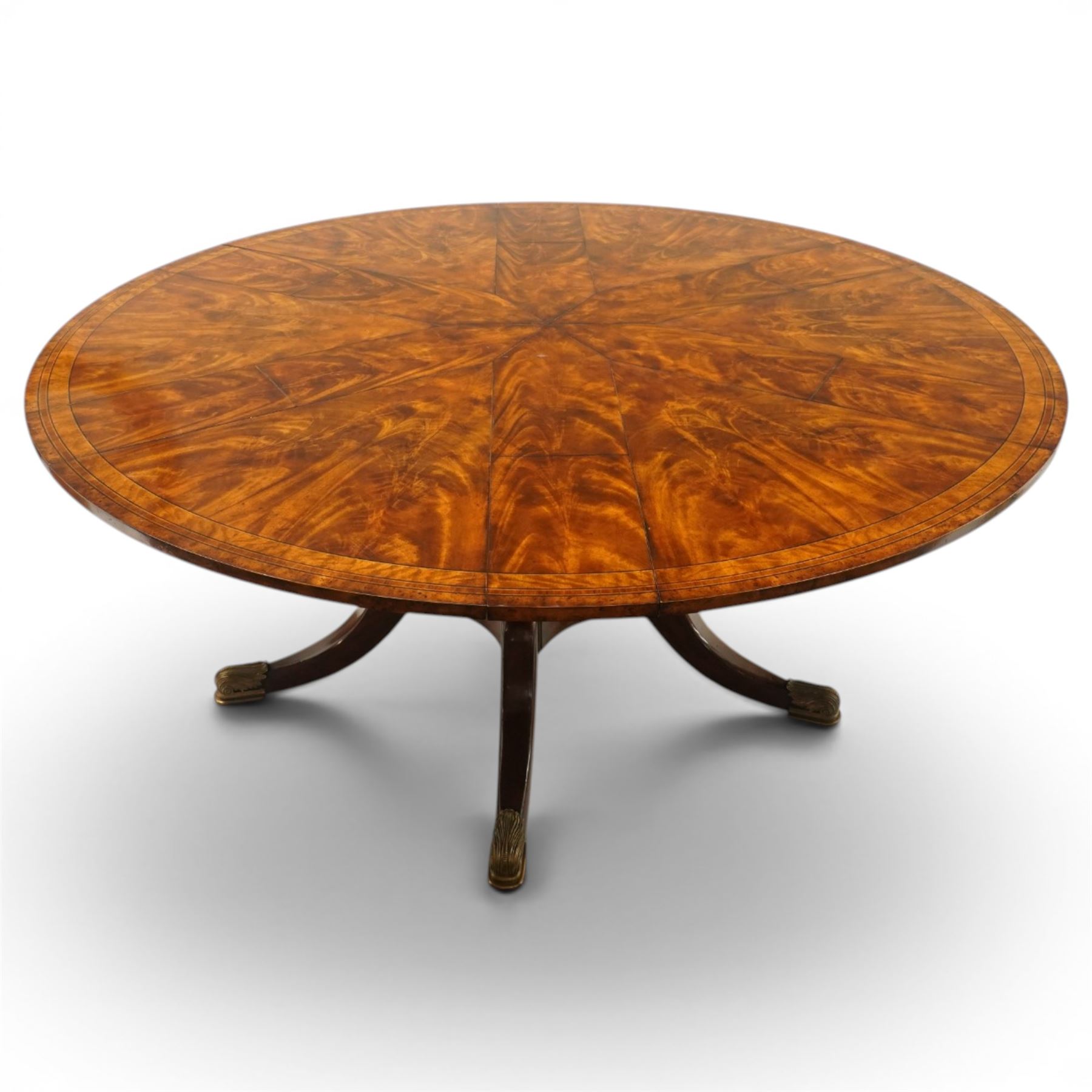 Theodore Alexander - Regency Revival figured mahogany 'Althorp Patent Jupe' extending dining table, the segmented circular top formed of six pull-out triangular divisions with inset fold-out leaves, raised on a large turned vasiform pedestal on a pentagonal platform base with ebonised stringing, terminating to five splayed supports with gilt metal acanthus scrolled feet, retailed by David Hick Interiors, Jersey