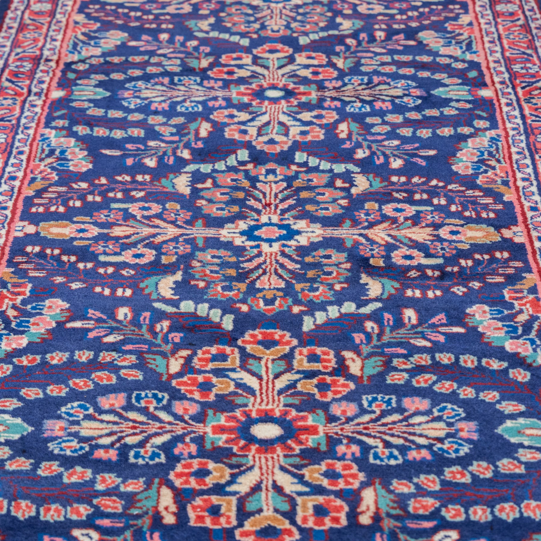North West Persian runner, the indigo field decorated with repeating symmetrical floral sprays, rosettes and curling foliage in coral, ivory and pale blue tones, enclosed by a red ground trailing flowerhead border and narrow patterned guard bands 