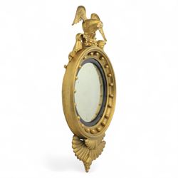 Early 20th-century Regency-style giltwood convex mirror, circular plate within a ball-mounted frame surmounted by an eagle cresting and flanked with scrolls, apron carved with foliate decoration 