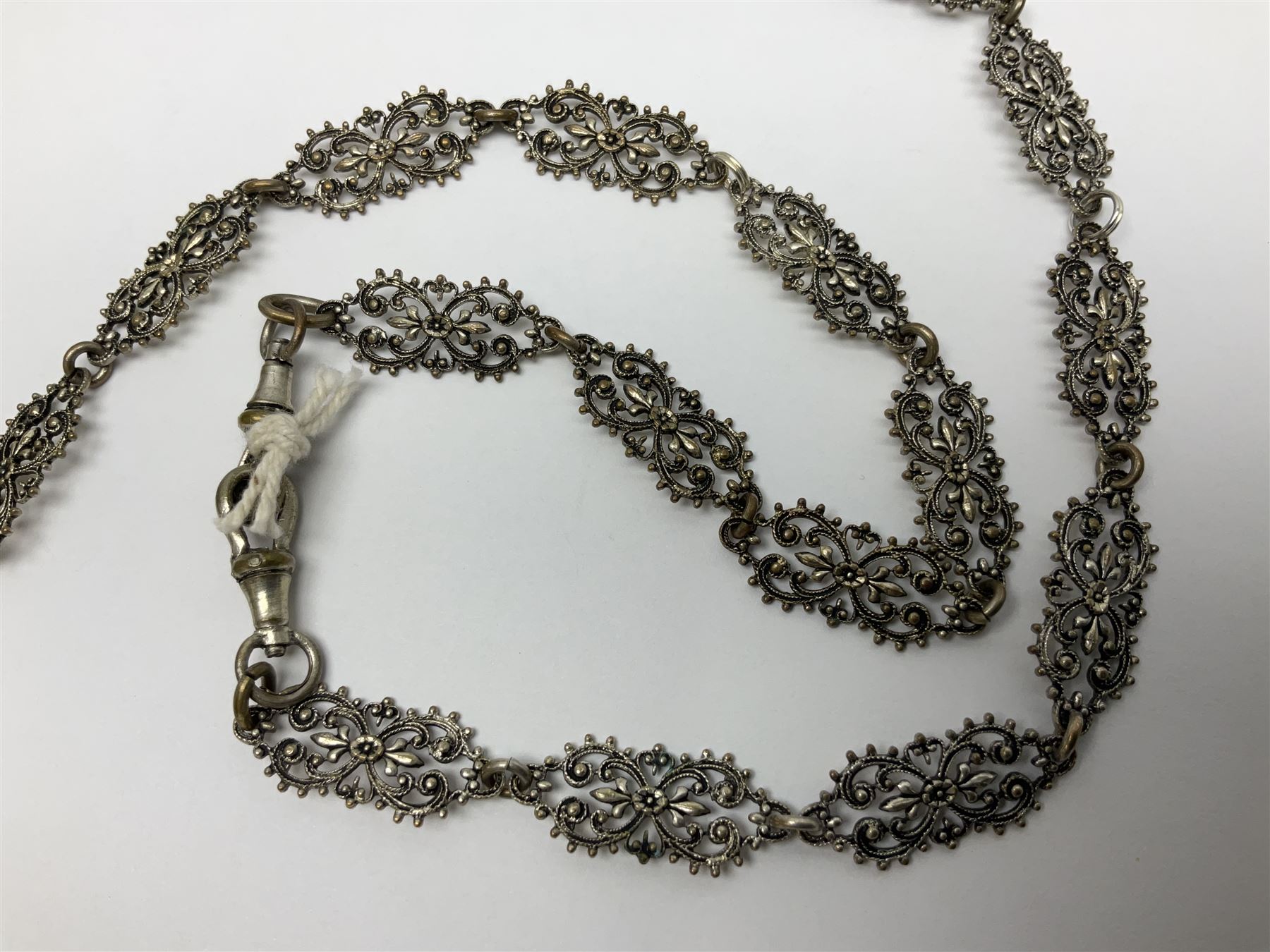 19th century continental silver plated chatelaine, the main body flanked with winged mythical beasts and central soldier slaying a dragon supporting three suspended items to include velvet lined small basket and long clasped filigree chain, together with a thimble