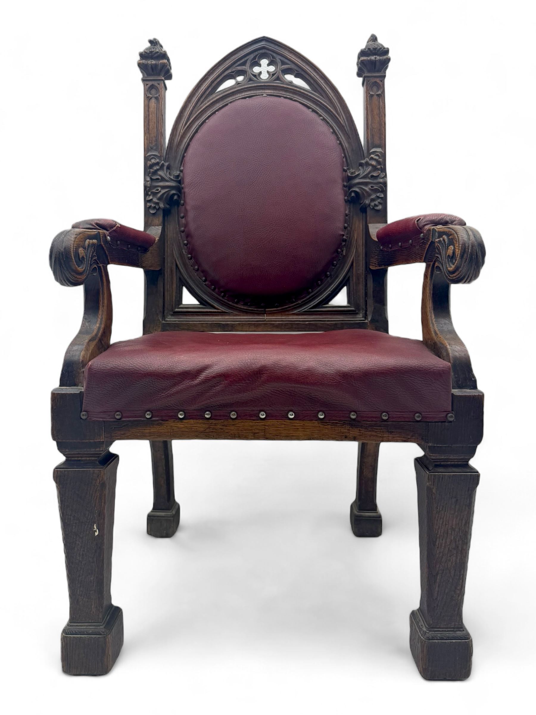 Late Victorian Gothic-revival armchair, arched crest rail carved with tracery and trefoil detail, padded circular back and seat, brass studded burgundy leather upholstery, shaped armrests with scrolled terminals, on square tapering supports