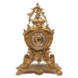 French-Late 19th century 8-day gilt brass rococo style mantel clock, c1890, waisted case  decorated with scroll work, leaves and musical instruments, resting on an attached plinth with splayed feet, dial within a glazed brass bezel with a gilt repoussé centre, porcelain cartouche Roman numerals and steel fleur-di-Lis hands, with a twin train movement, recoil anchor escapement and countwheel strike, sounding the hours and half-hours on a bell. With a matching pair of five-light candelabra. No Pendulum or Key.