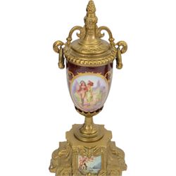 Continental-20th century clock garni in a mid 19th century style case, with porcelain panels and dial, spring driven two train movement with a floating balance escapement, striking the hours and half hours on two bells. With conforming urns. 