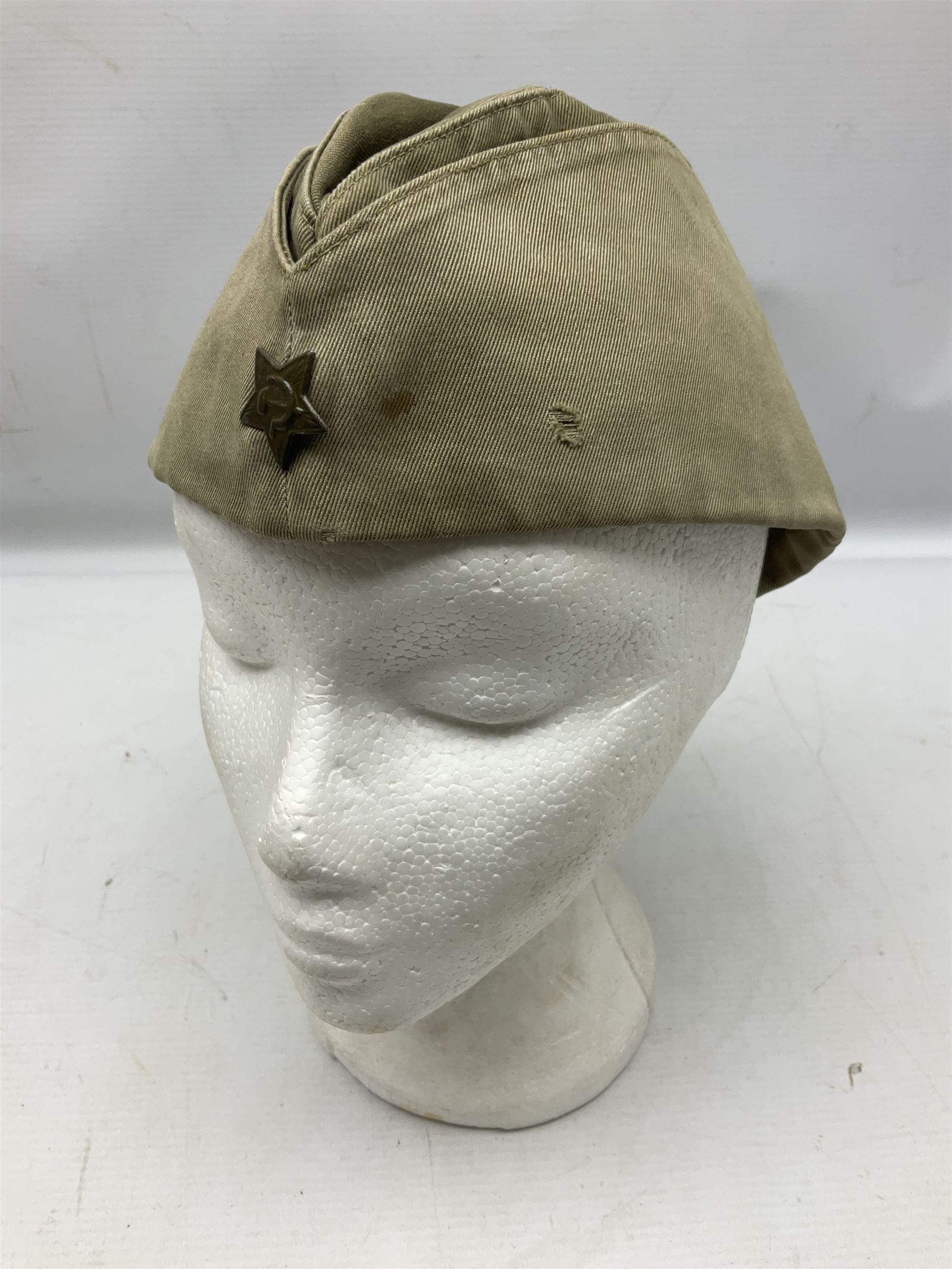 Four side caps - WW2 Russian, post-WW2 Russian and two East German; all with badges, one with multiple metal badges (4)