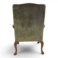 Pair of Georgian style wing armchairs, upholstered in green velvet, each with shaped wing backs, padded scroll arms and loose seat cushions, raised on cabriole supports terminating in pad feet, one with tasselled fringe