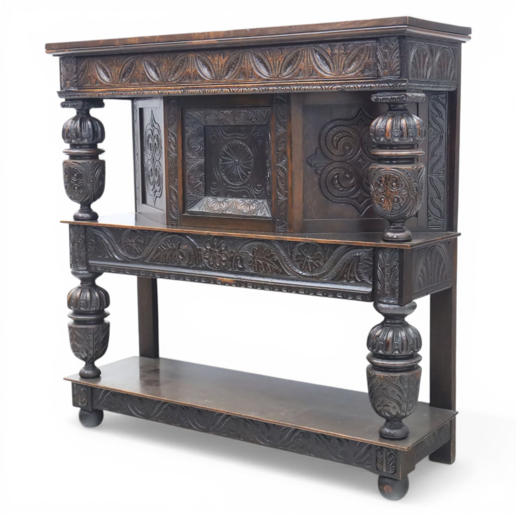 Jacobean revival oak side cabinet, rectangular top above carved frieze of stylised foliage and lunettes, fitted with a central cupboard doors with applied carved panels, above a frieze drawer, supported on turned and carved vase-shaped supports, united by stretcher tier and lower shelf